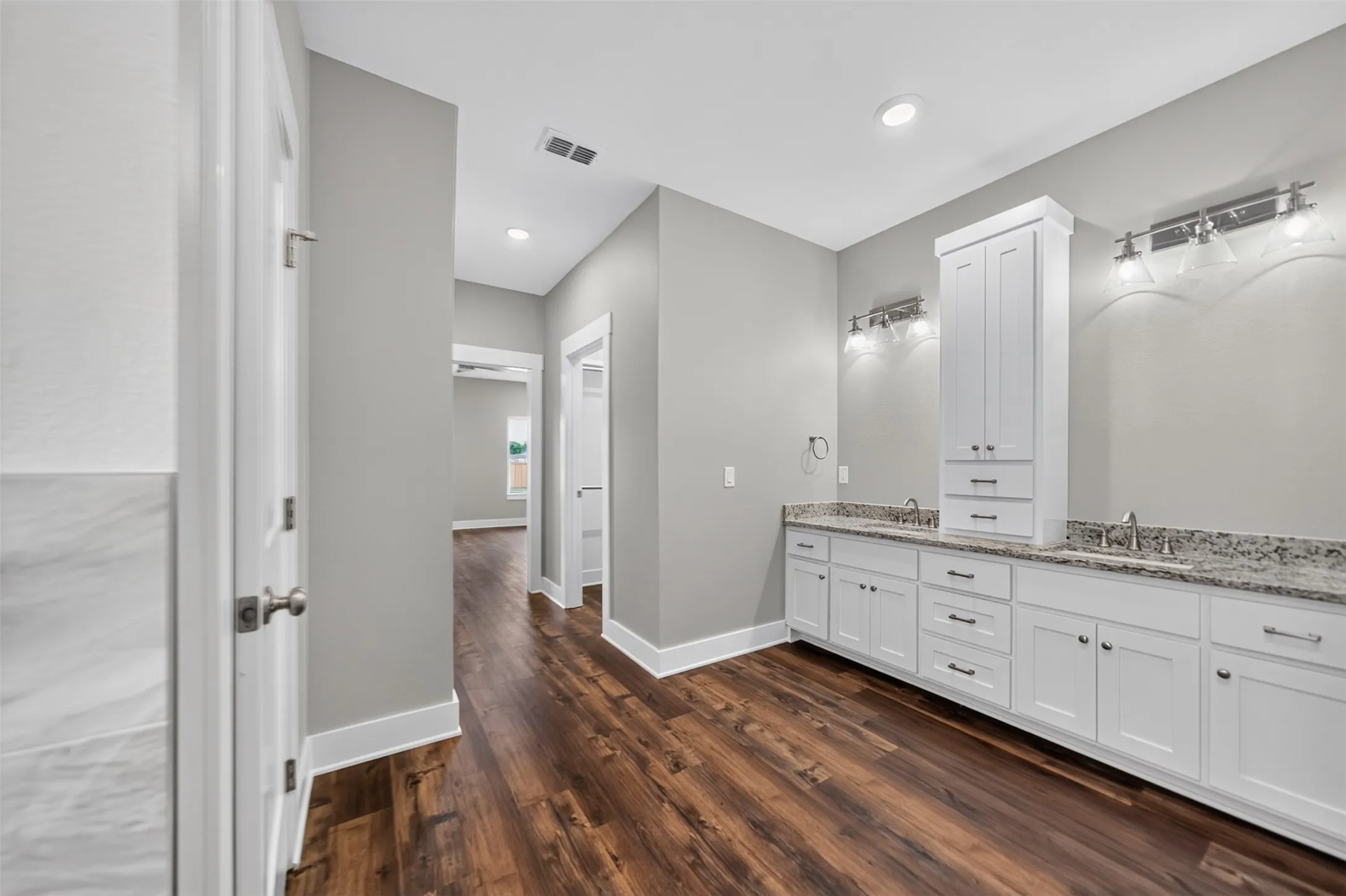 Spacious vanity area featuring white cabinetry, granite-finish countertops, dual sinks, and wood-finish flooring