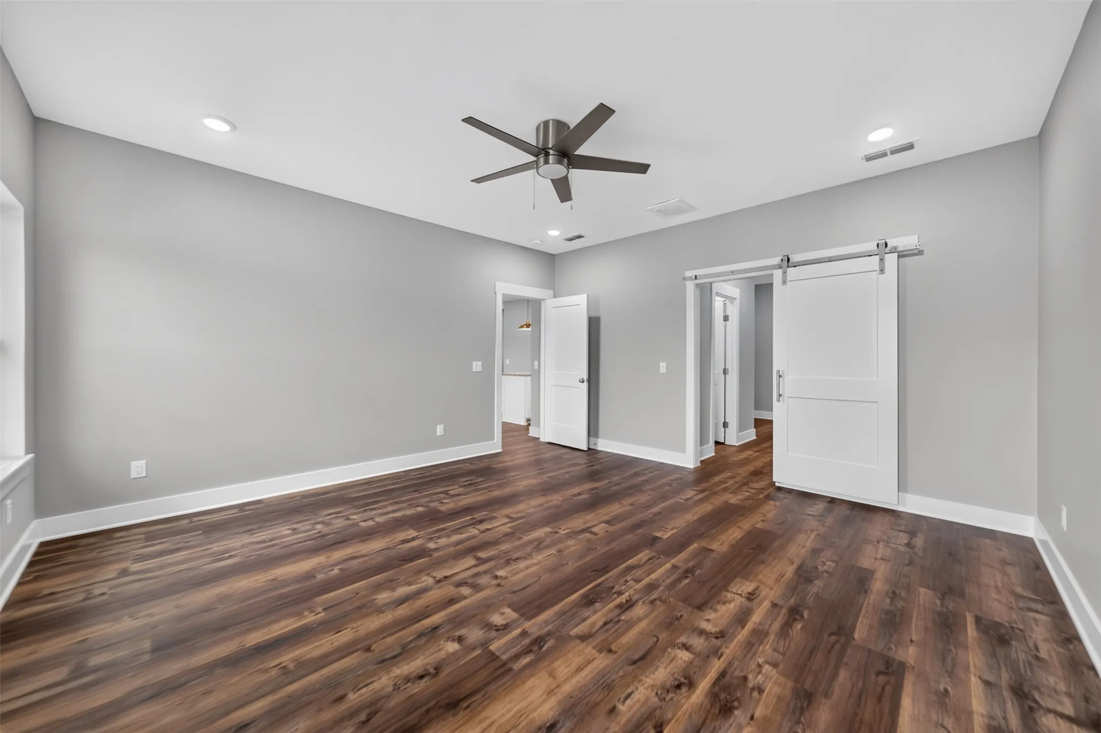 Spacious room featuring rich wood-finish flooring, light gray walls, and recessed lighting
