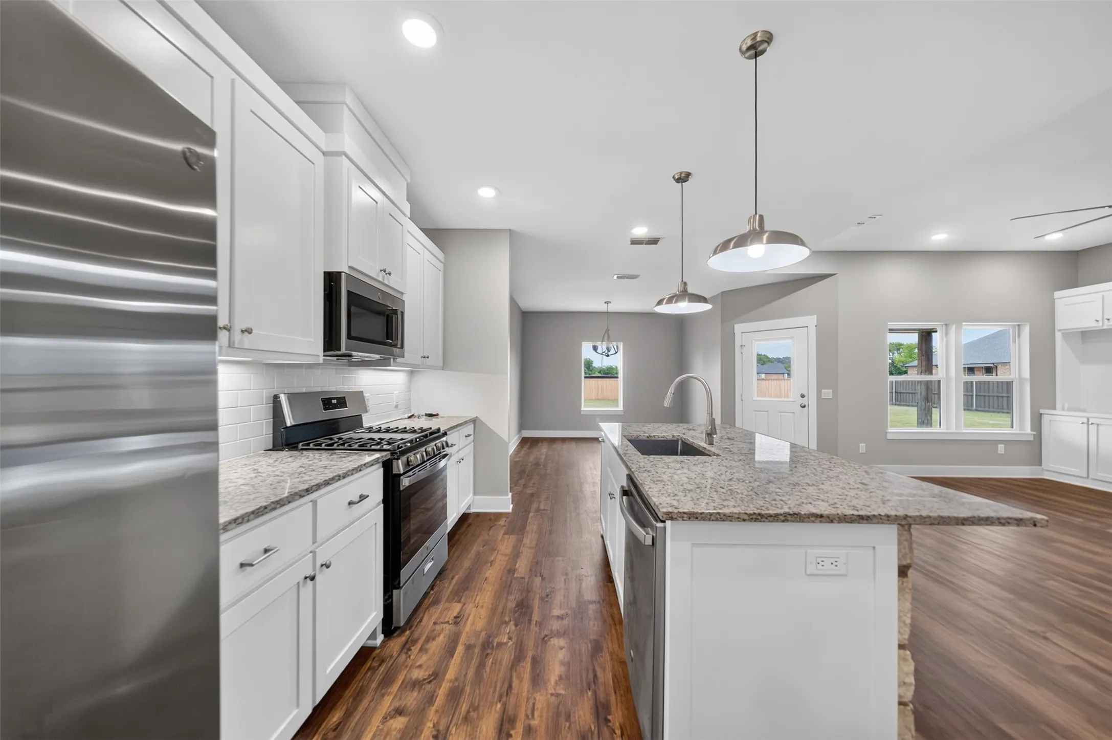 Open-concept kitchen featuring white shaker cabinetry, stainless steel appliances, granite countertops, and wood-finish flooring
