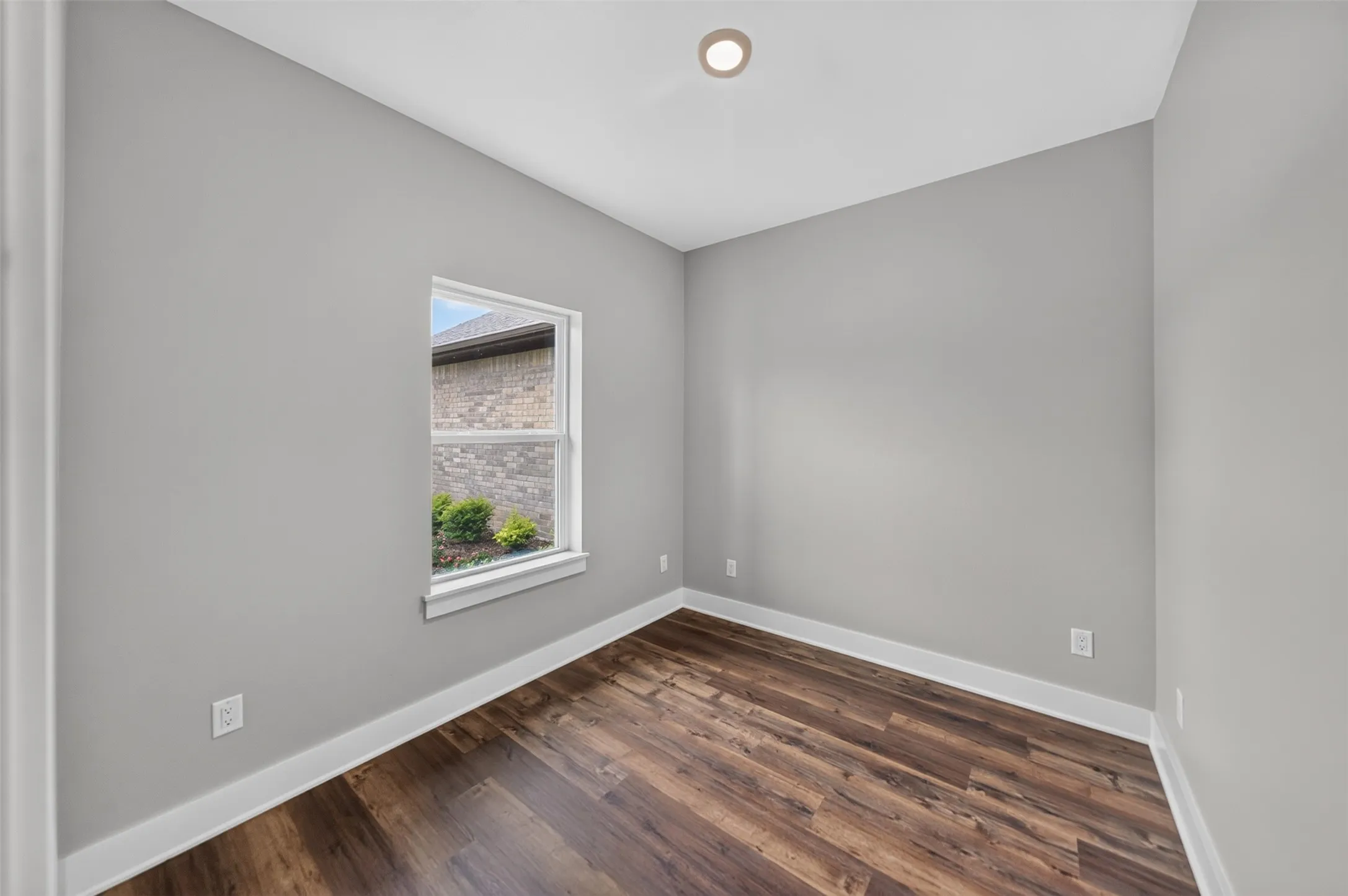 Room with neutral gray walls, wood-finish flooring, recessed ceiling light, and white trim