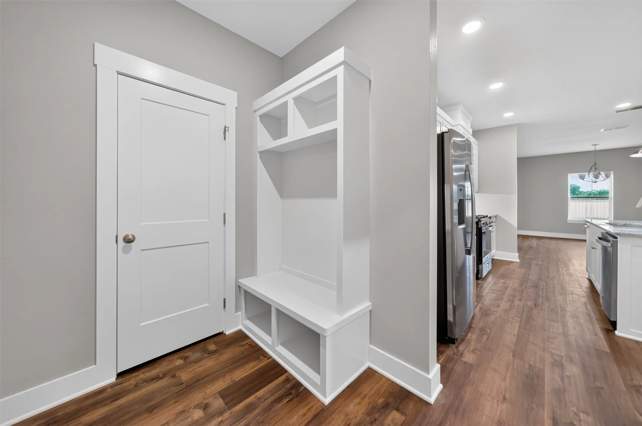 Built-in white storage bench with open shelving, wood-finish flooring, white baseboards, and a modern two-panel door