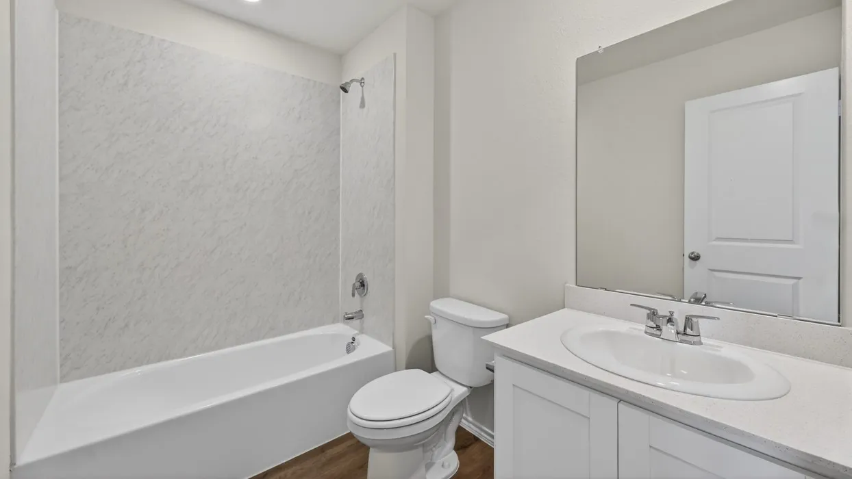 Bathroom featuring a white vanity with an undermount sink, a large mirror, a white toilet, and a bathtub with a patterned surround