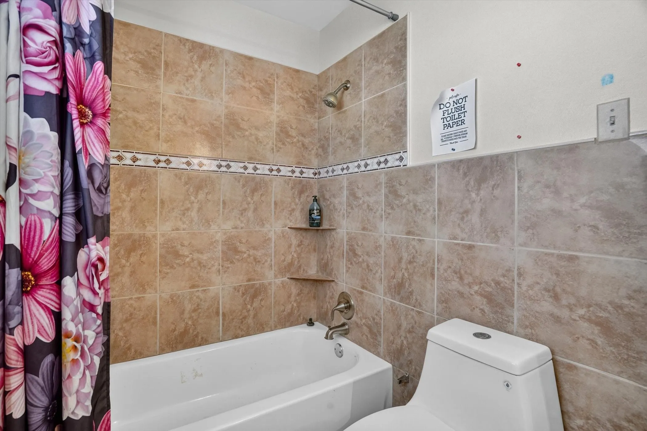 Bathroom featuring a tiled shower surround with decorative accent tile, built-in shower shelves, and a shower/tub combination