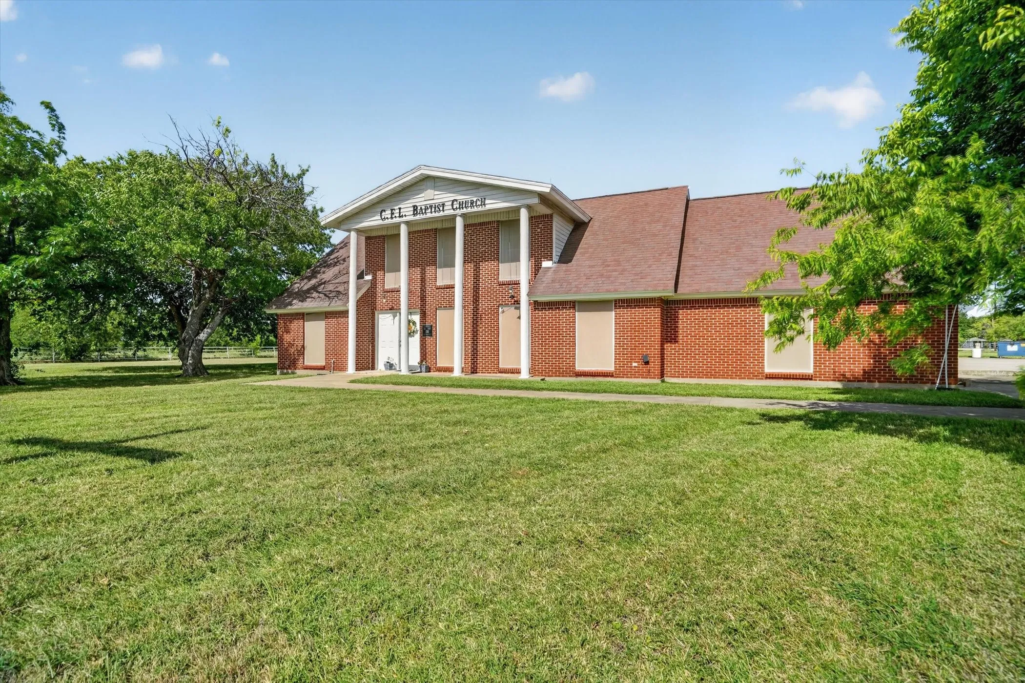 Red brick building with a columned portico entrance, featuring a brown shingle roof and a concrete pathway