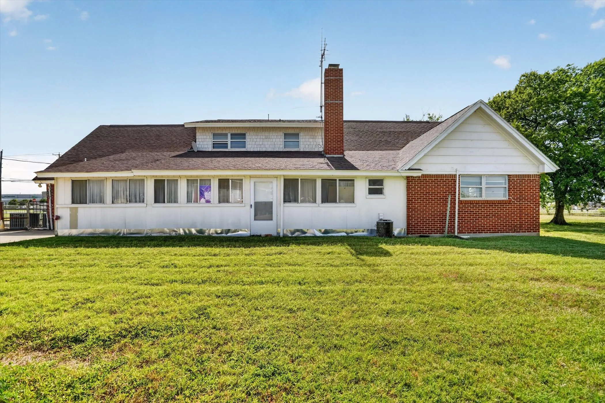Expansive grassy yard with a multi-level home featuring a brick chimney, dormer windows, and a combination of brick and white siding