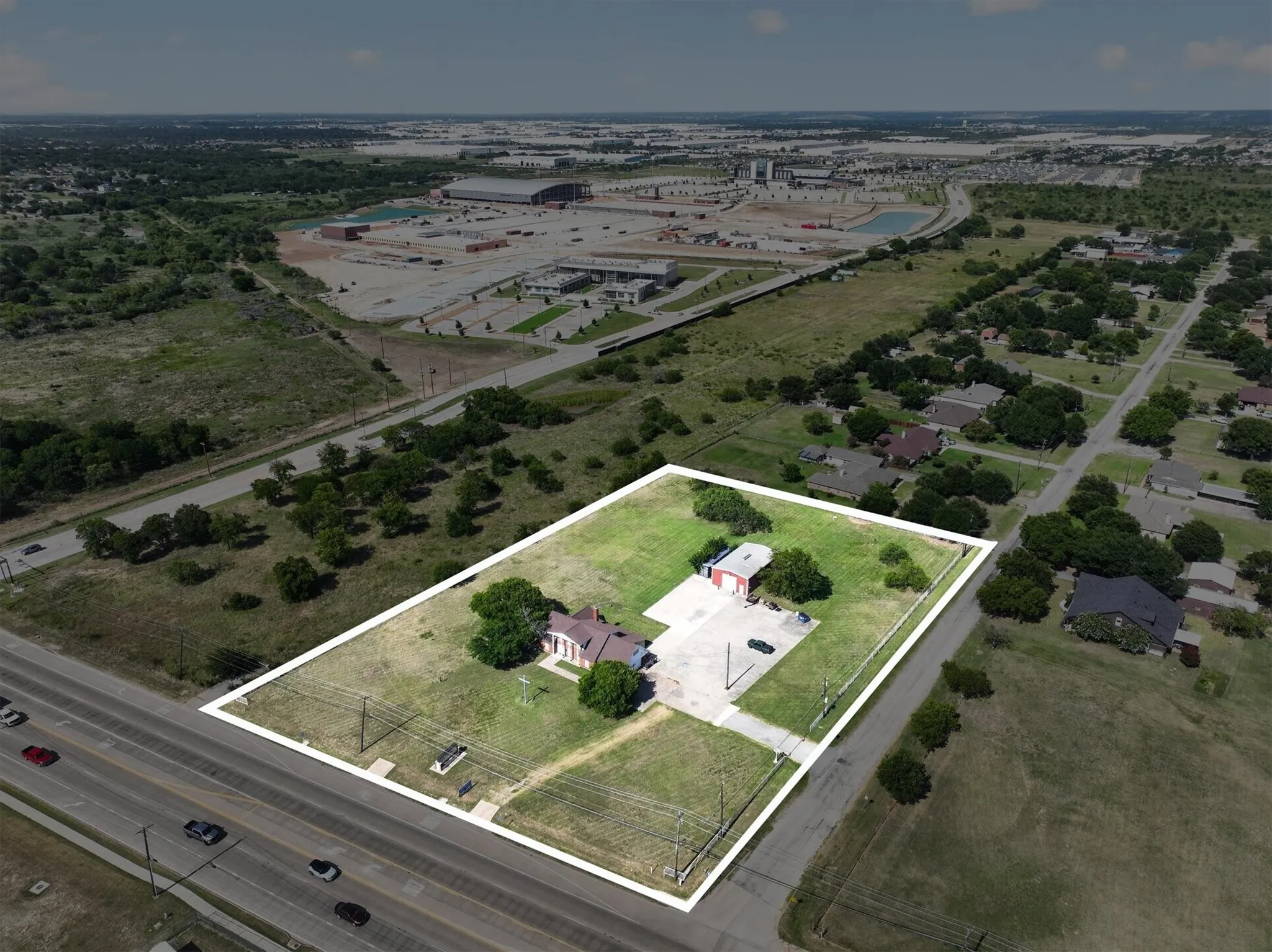 Expansive property featuring a red brick structure with a detached garage building, extensive paved areas, and mature trees
