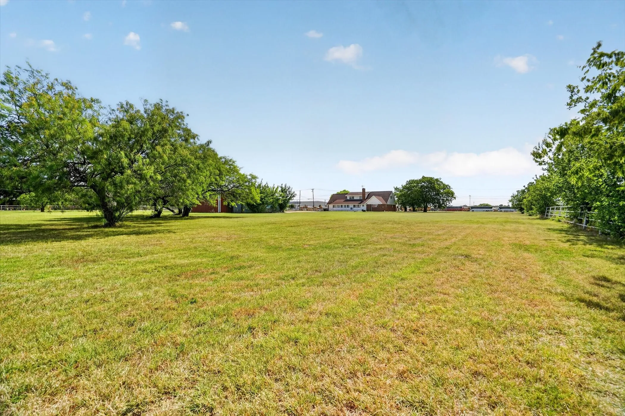 Expansive grassy land featuring mature trees and a distant residential structure