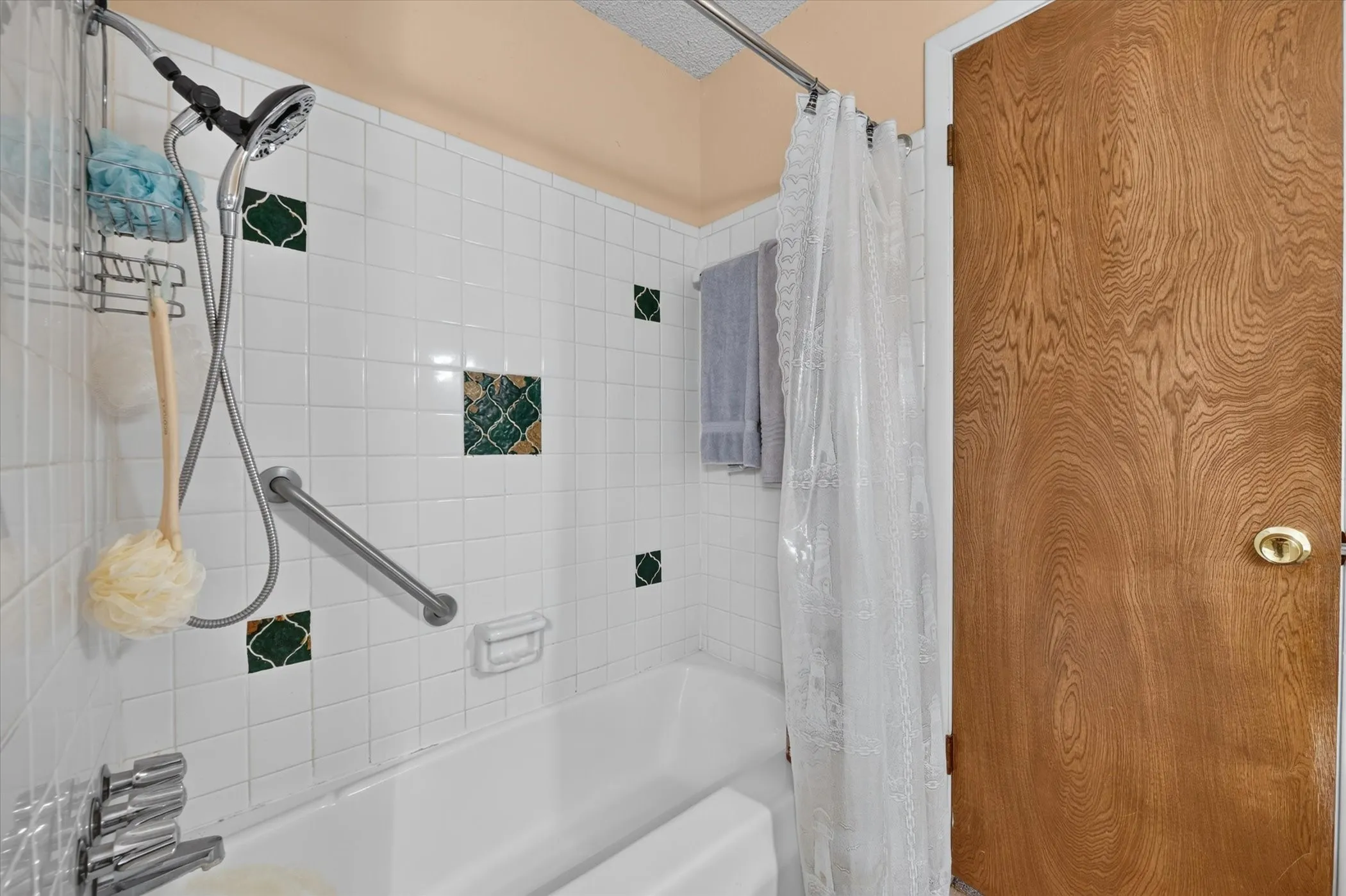 Bathroom featuring a white bathtub with chrome fixtures, white subway tile surround, decorative green accent tiles, and a shower curtain rod