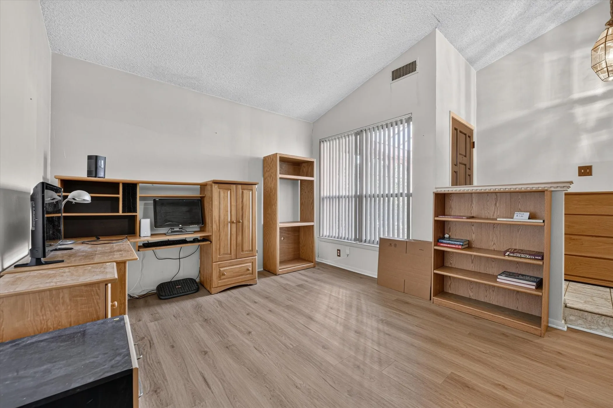 Spacious interior featuring wood-finish flooring, vaulted ceilings, and a large window with vertical blinds
