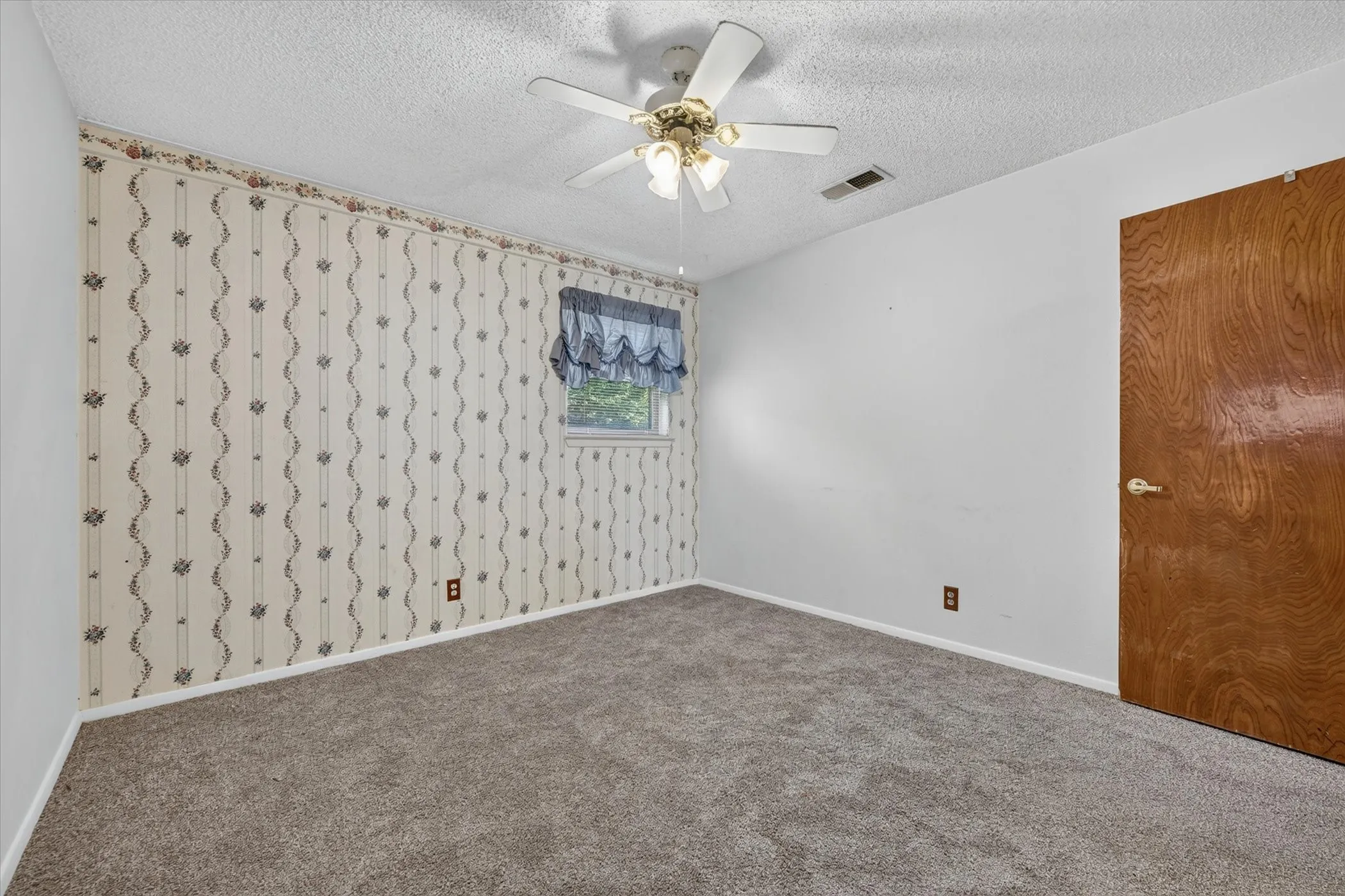 Carpeted room featuring a ceiling fan, a window with a valance, and a wood-paneled door
