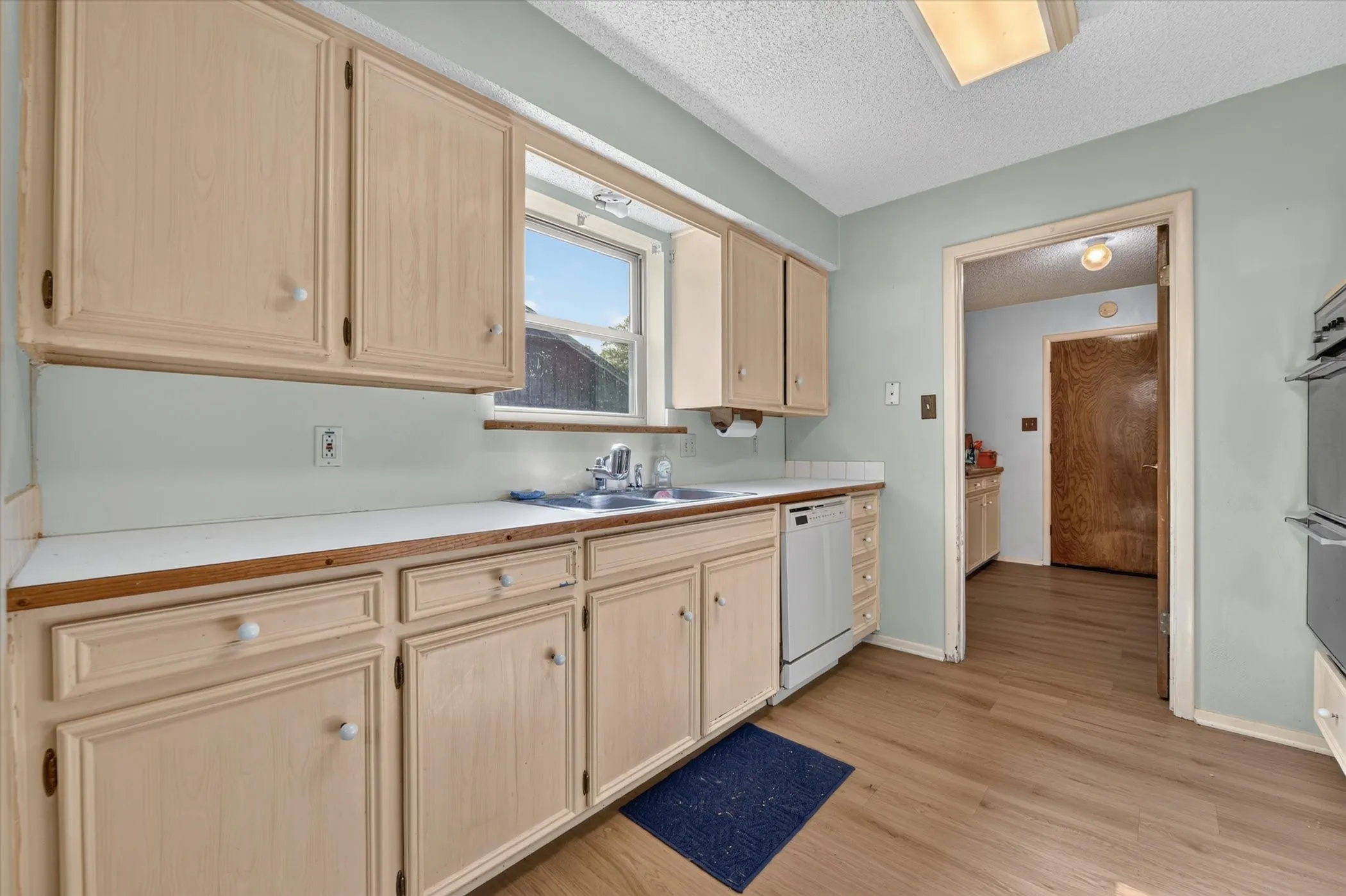 Kitchen featuring wood-finish flooring, light-toned cabinetry, light countertops, a double basin sink, and a built-in dishwasher