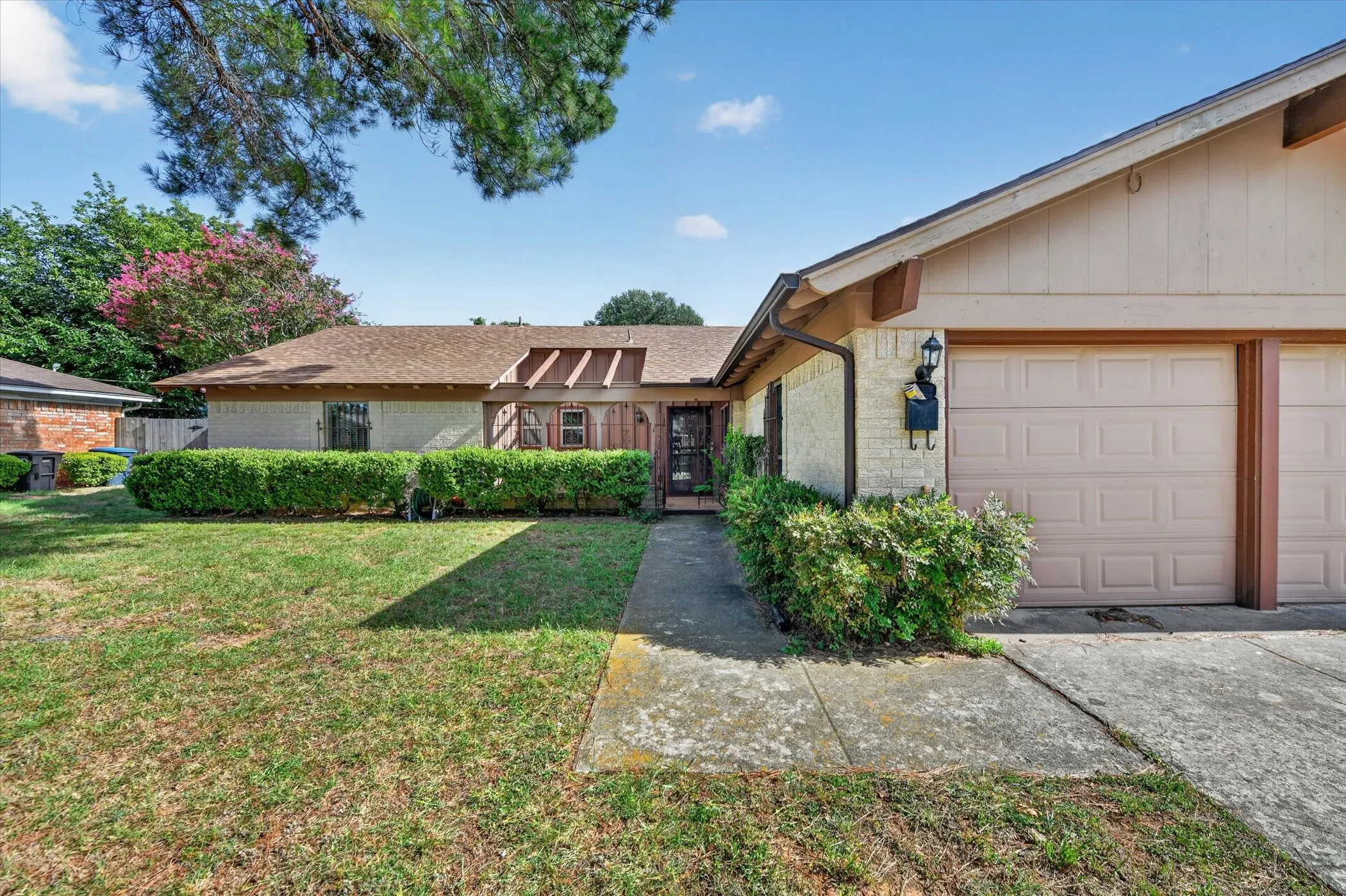Residential exterior featuring a two-car garage, brick facade accents, a concrete driveway, and a front walkway