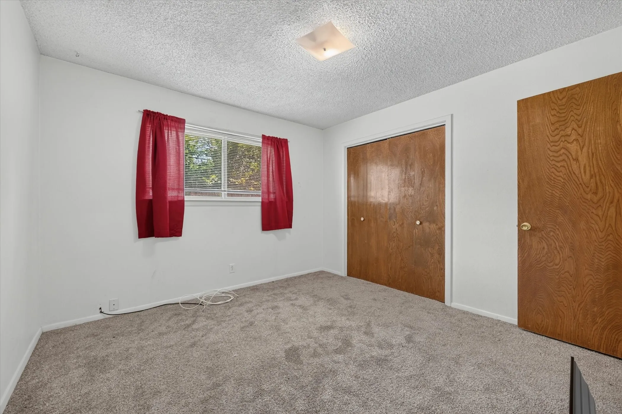 Carpeted room featuring a double-pane window, wood-finish bi-fold closet doors, a single wood-finish door, white walls, and a ceiling-mounted light fixture
