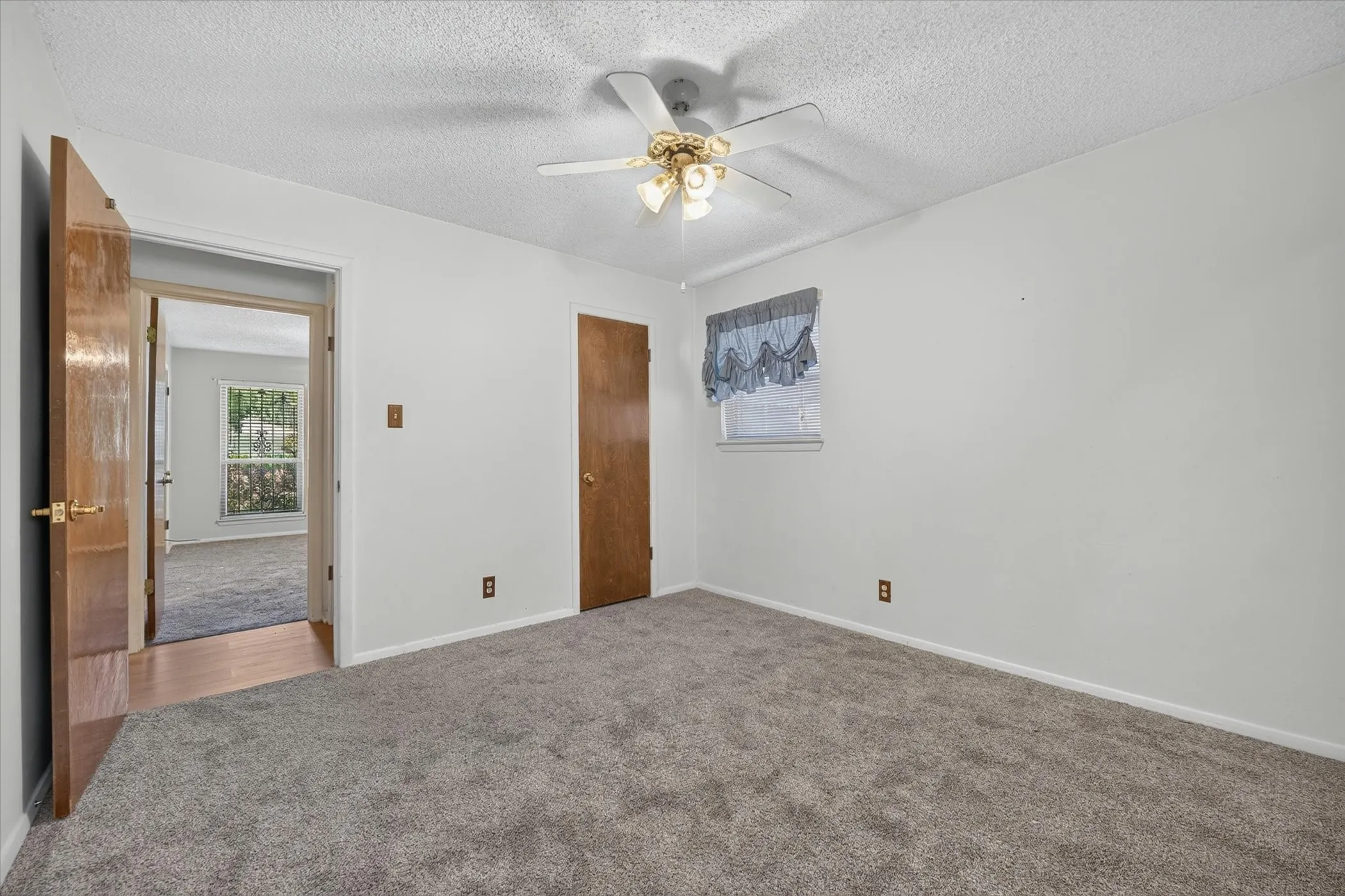 Carpeted room featuring a ceiling fan with integrated lighting, a window with a valance, and solid core doors with brass hardware