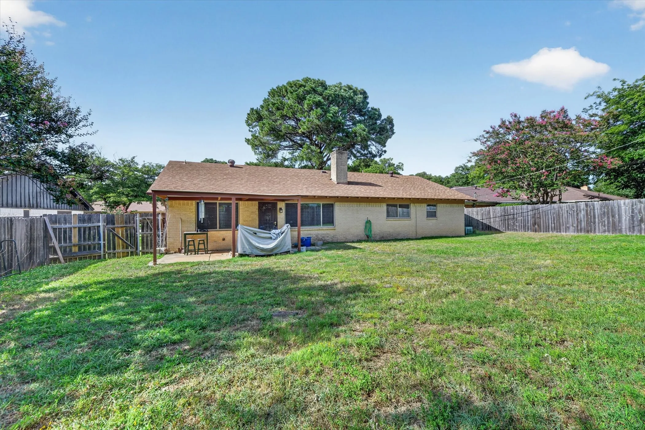 Expansive backyard featuring a large green lawn, wood privacy fencing, and mature trees