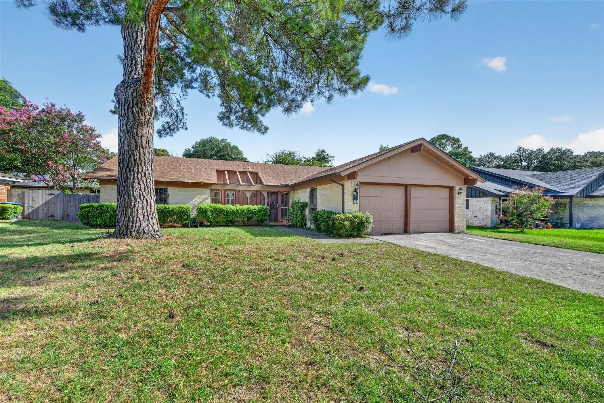 Single-story residence featuring a two-car garage with wood-finish doors, a pitched roof, and a mature tree providing shade to the front lawn