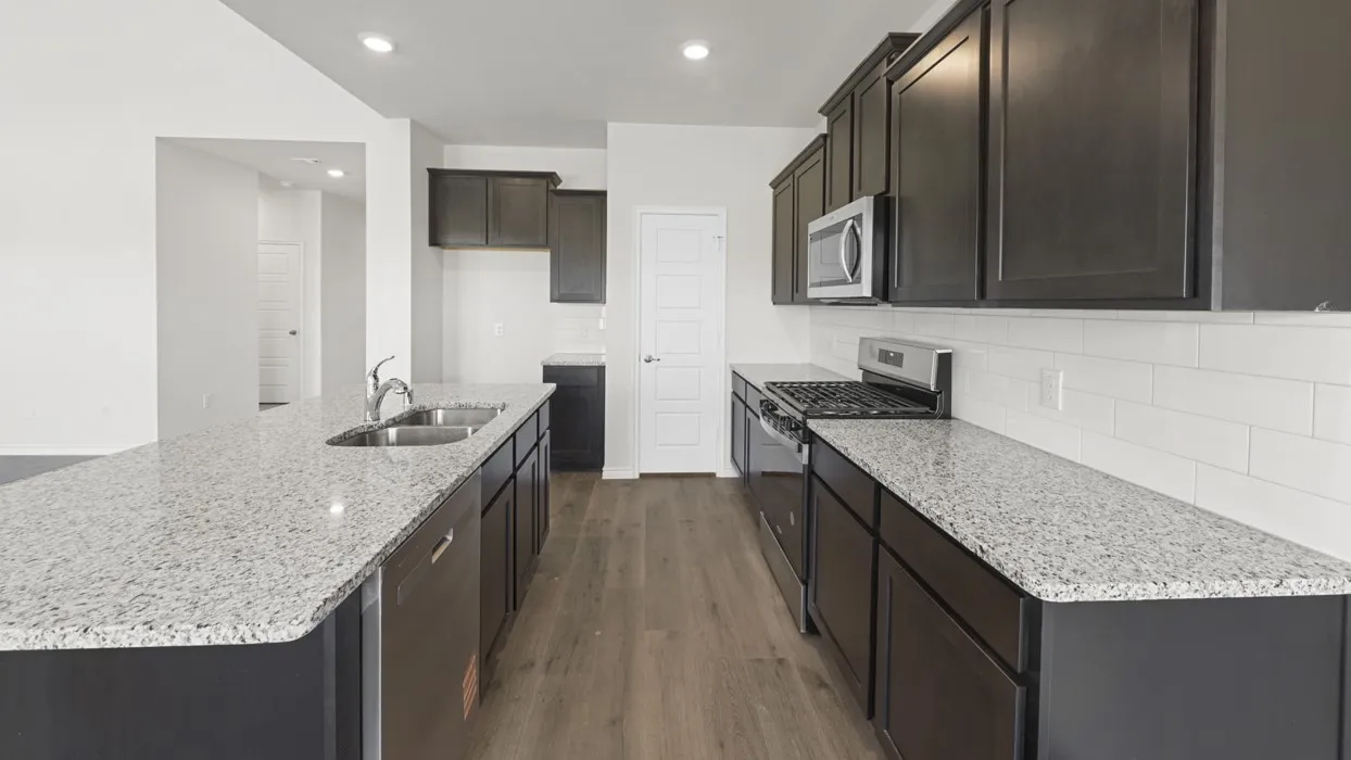 Kitchen featuring an expansive island with a dual-basin sink, granite countertops, dark wood cabinetry, stainless steel appliances, and wood-finish flooring