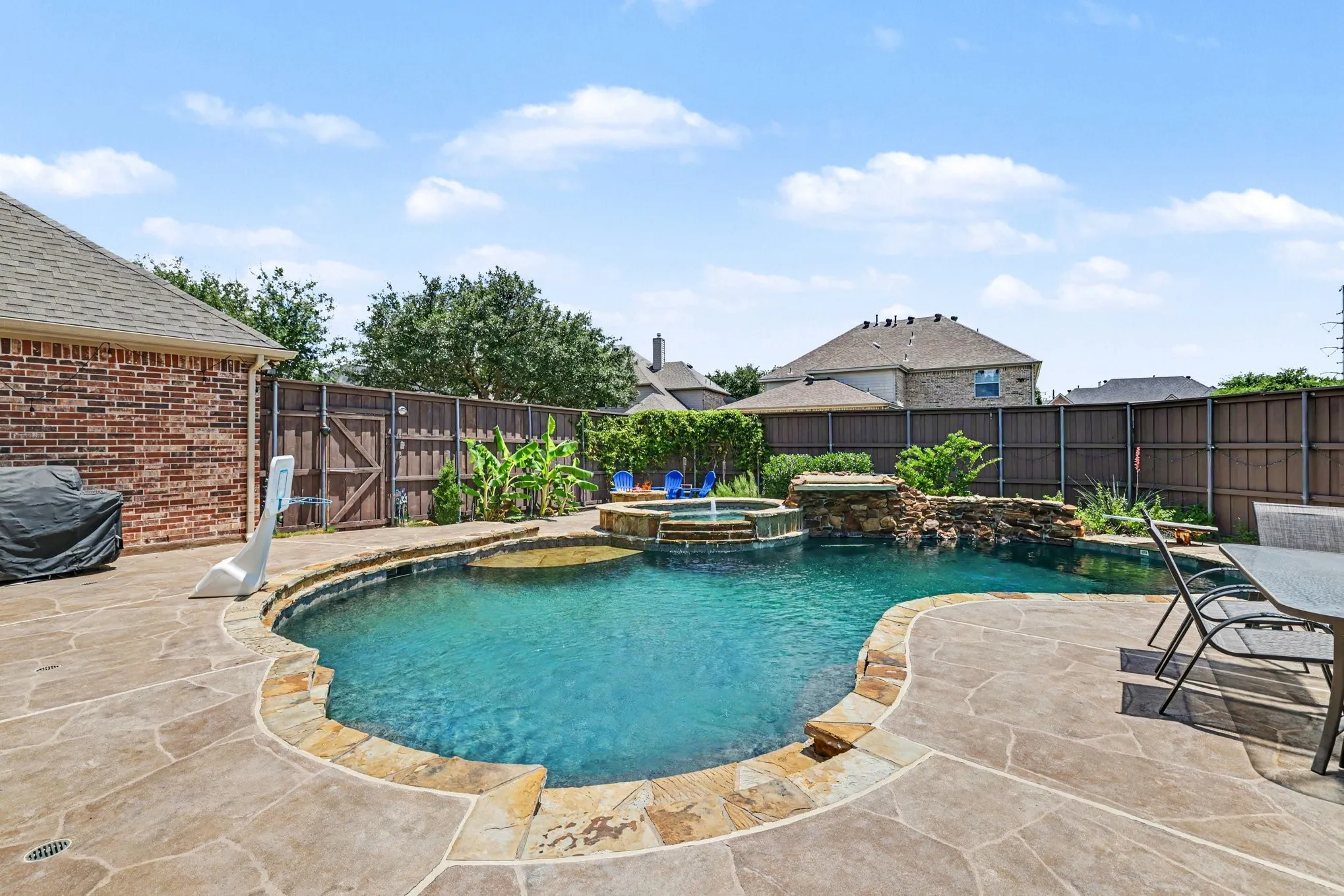 Freeform swimming pool featuring a stone surround, integrated spa, and rock waterfall