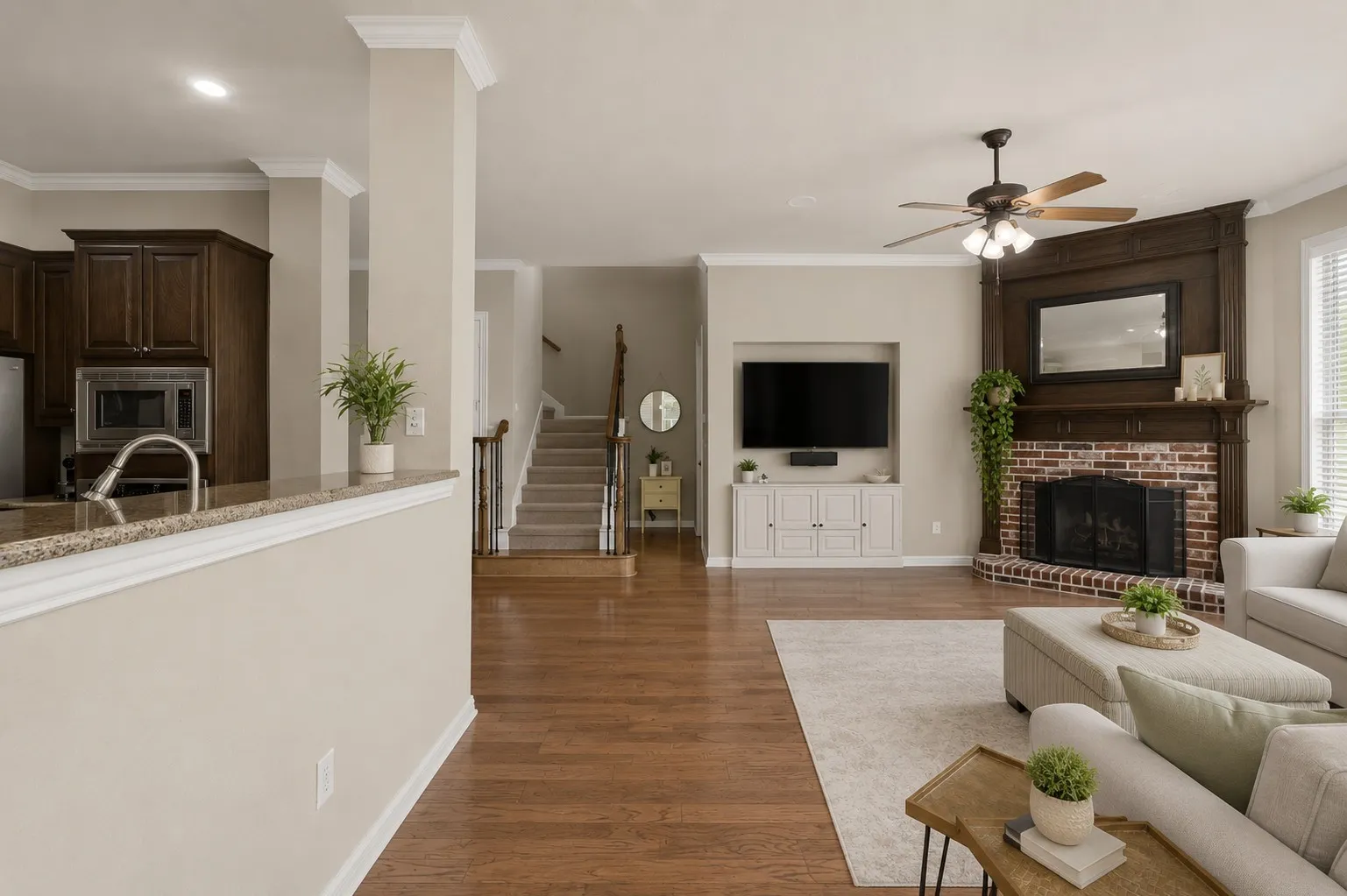 Hardwood flooring throughout, brick fireplace with decorative wood mantel, built-in media console, wood-finish cabinetry, and a ceiling fan