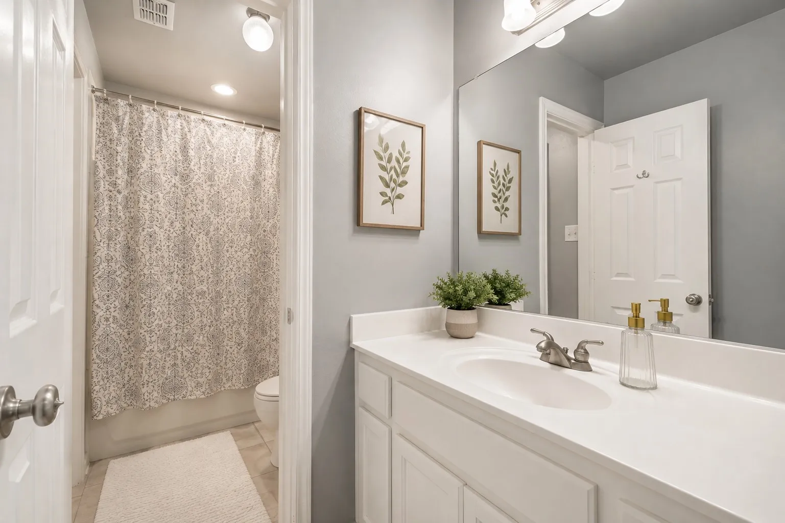 White vanity with integrated sink, brushed nickel faucet, large wall mirror, and overhead vanity lighting