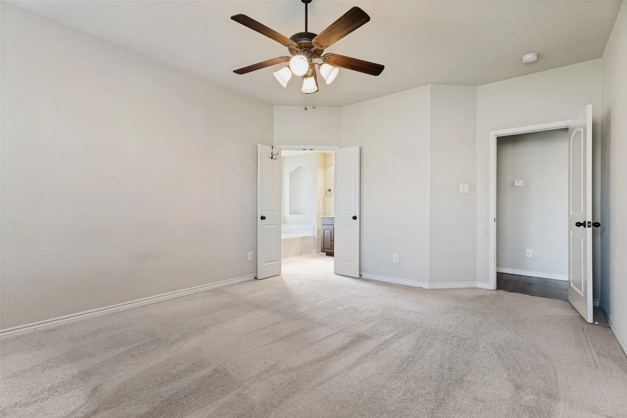 Spacious carpeted room featuring a ceiling fan with integrated lighting, two panel doors, and neutral wall tones