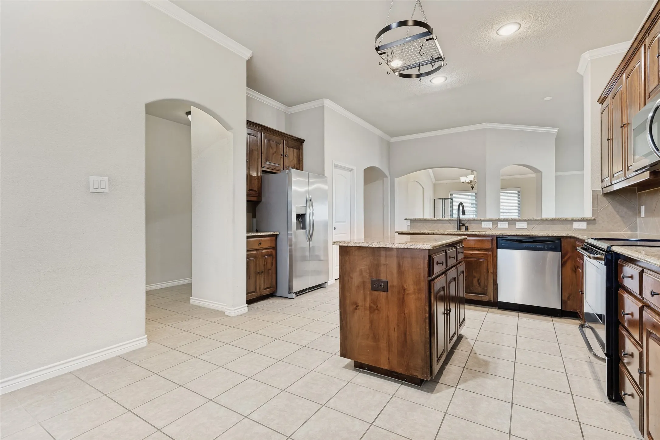 Kitchen featuring tile flooring, a central island, wood-finish cabinetry, stainless steel appliances, and light-toned countertops