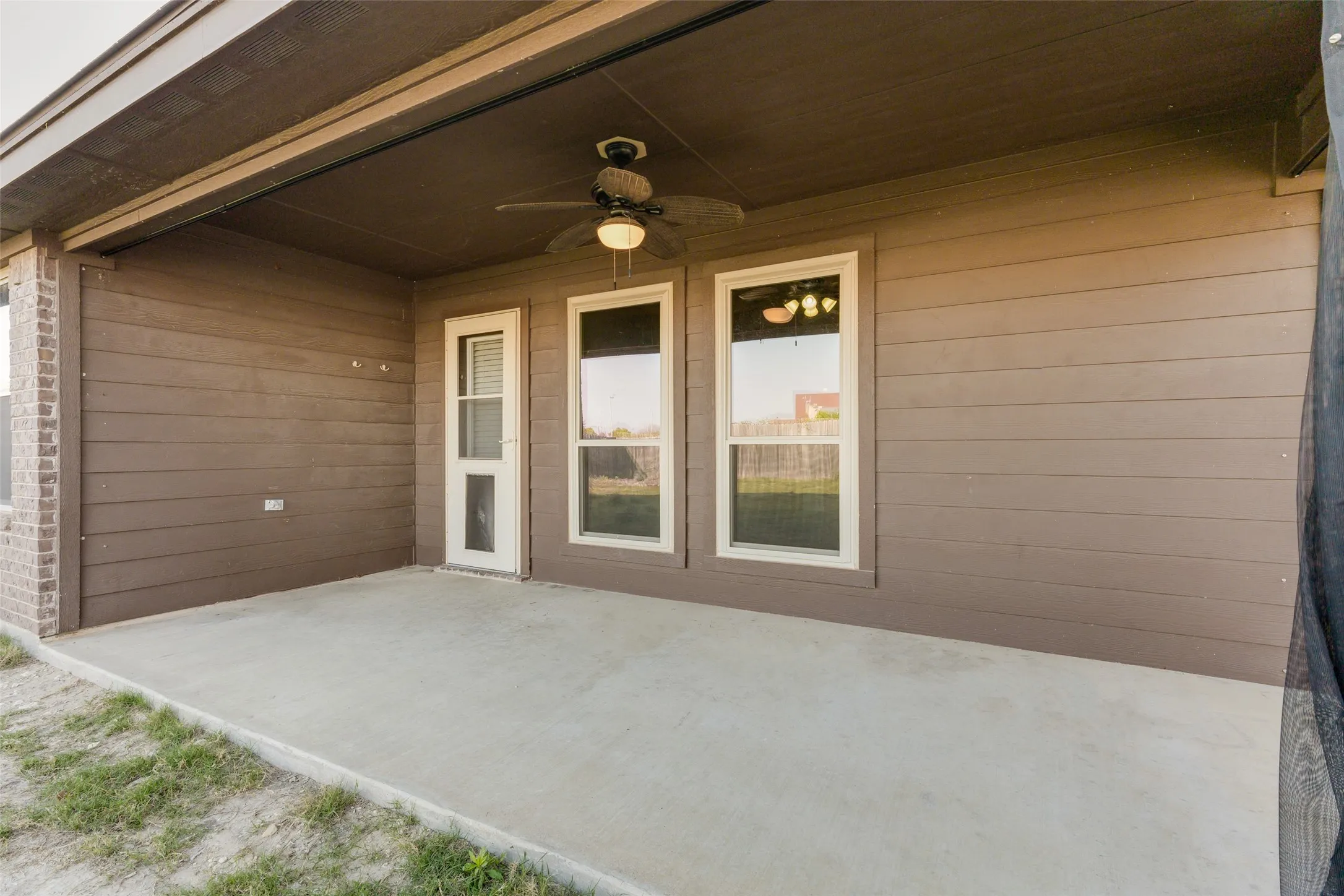 Covered concrete patio featuring a ceiling fan with integrated lighting, brown siding, and brick accents