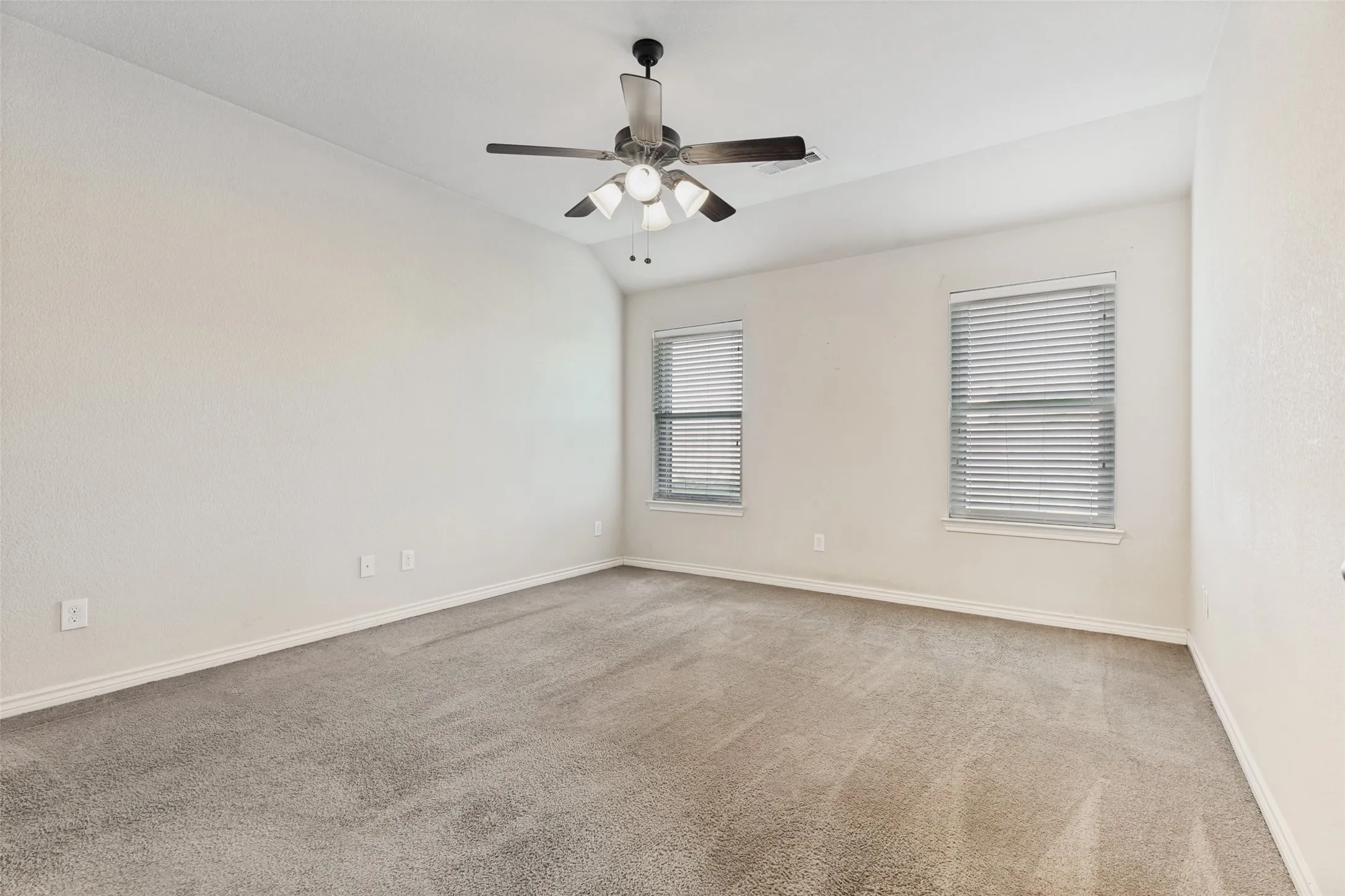 Carpeted room featuring a ceiling fan with integrated lighting, two windows with blinds, and light-colored walls