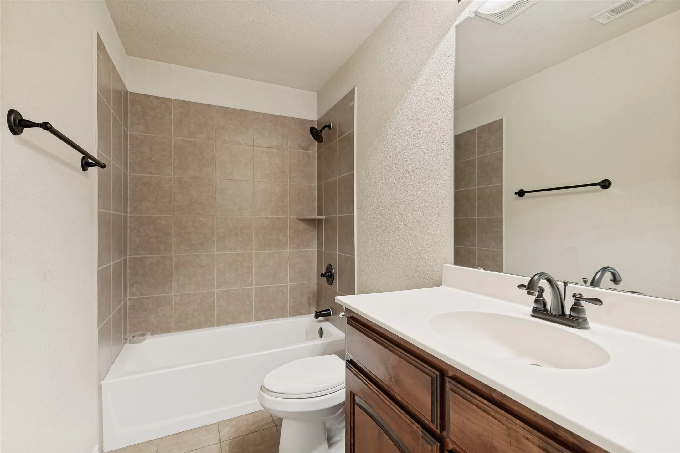Bathroom featuring a white bathtub, tiled shower surround with built-in shelf, dark bronze fixtures, and a vanity with a white countertop and wood-finish cabinetry