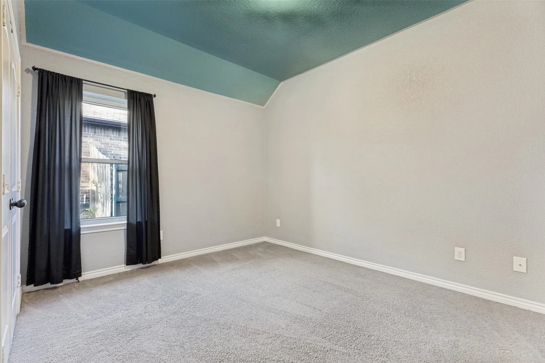 Carpeted room featuring a window with dark drapery, light grey wall paint, white baseboards, and a vaulted ceiling with a blue finish