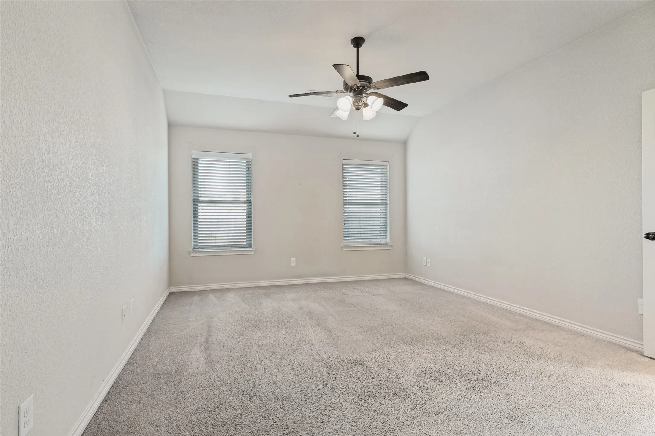 Carpeted room featuring a ceiling fan with integrated lighting, two windows with horizontal blinds, and clean white baseboards