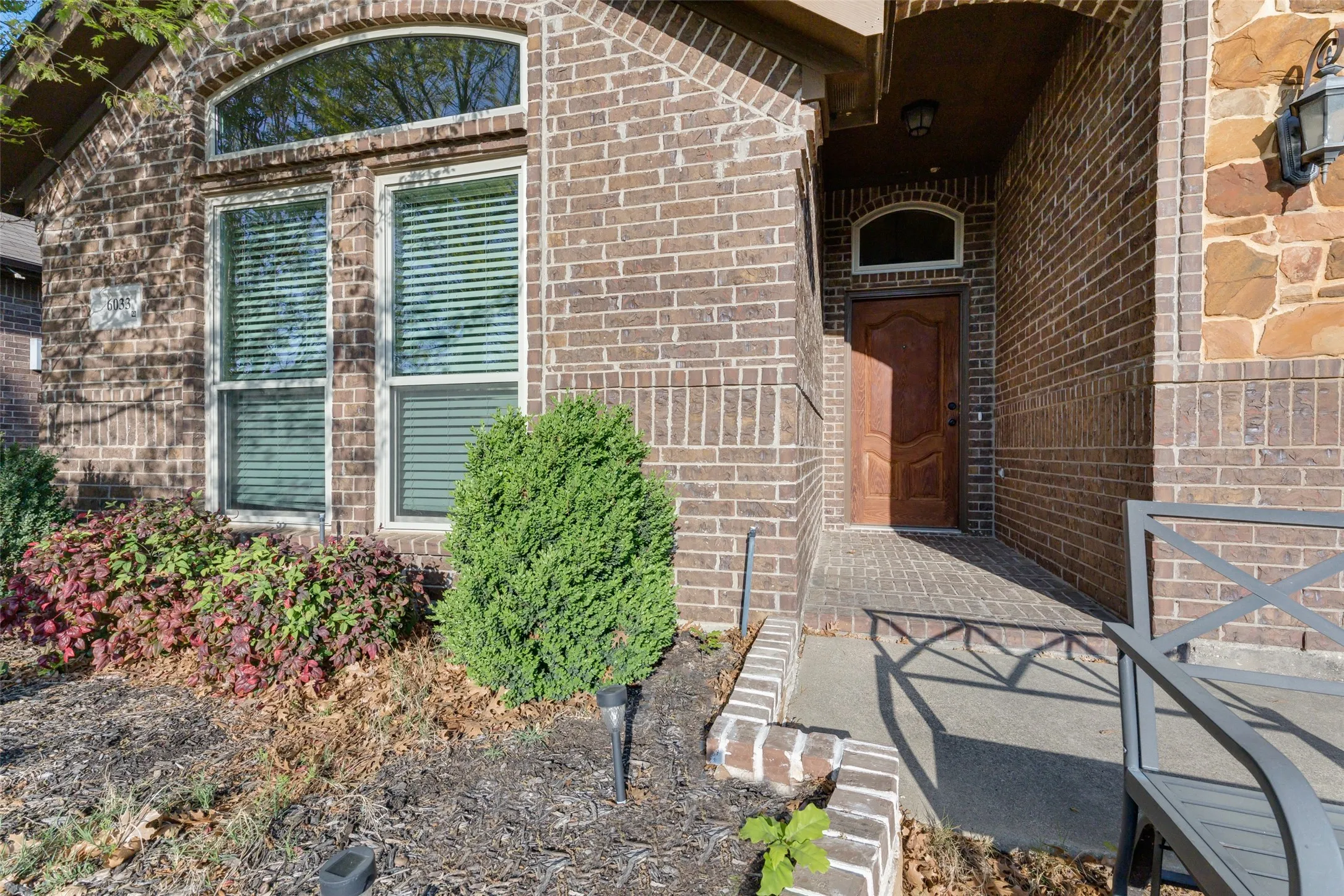 Brick exterior facade featuring a recessed entry with a wood-finish door, arched transom window, and stone accents
