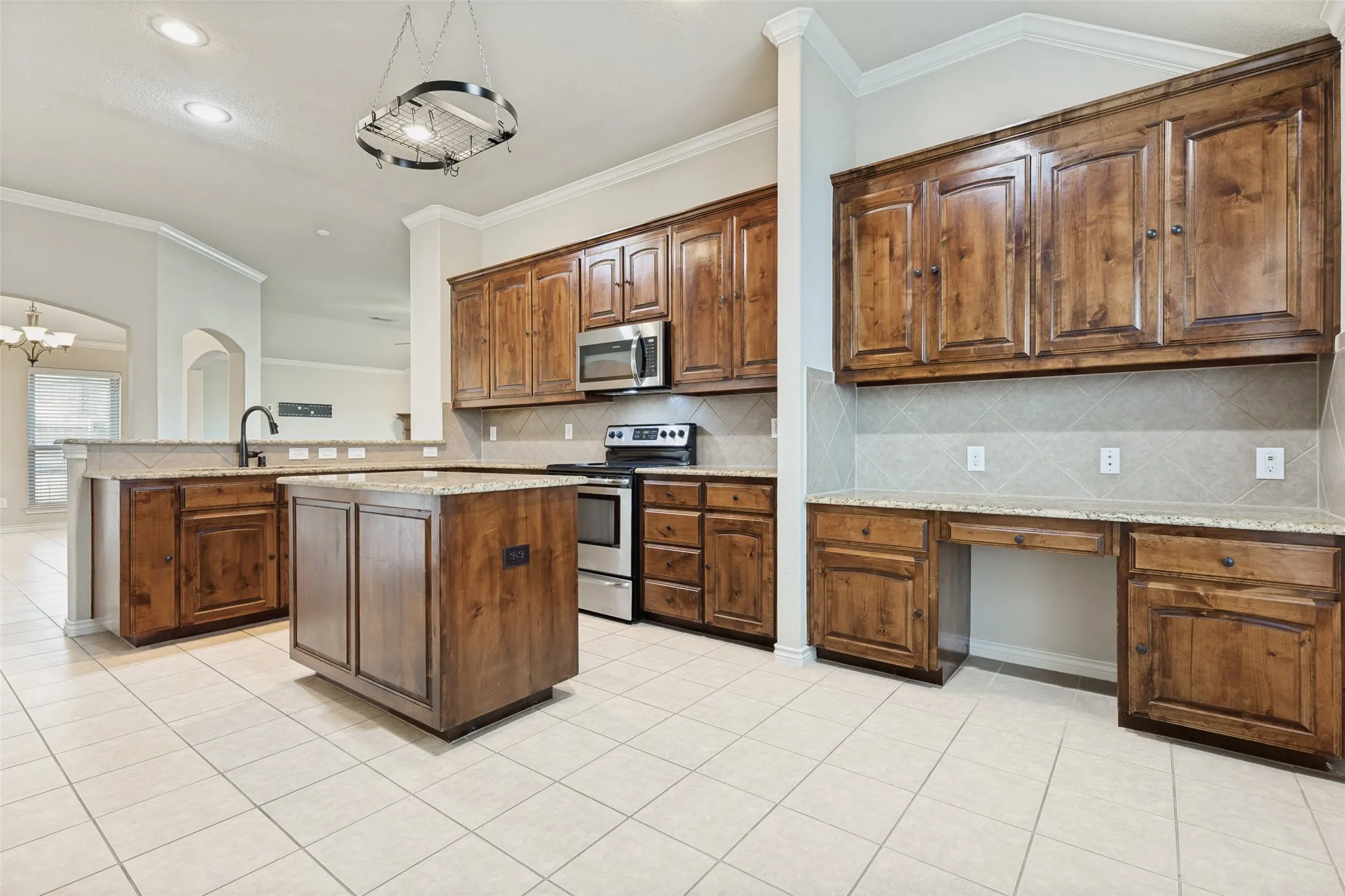 Spacious kitchen featuring extensive wood cabinetry, granite countertops, a central island, stainless steel appliances, and tile flooring