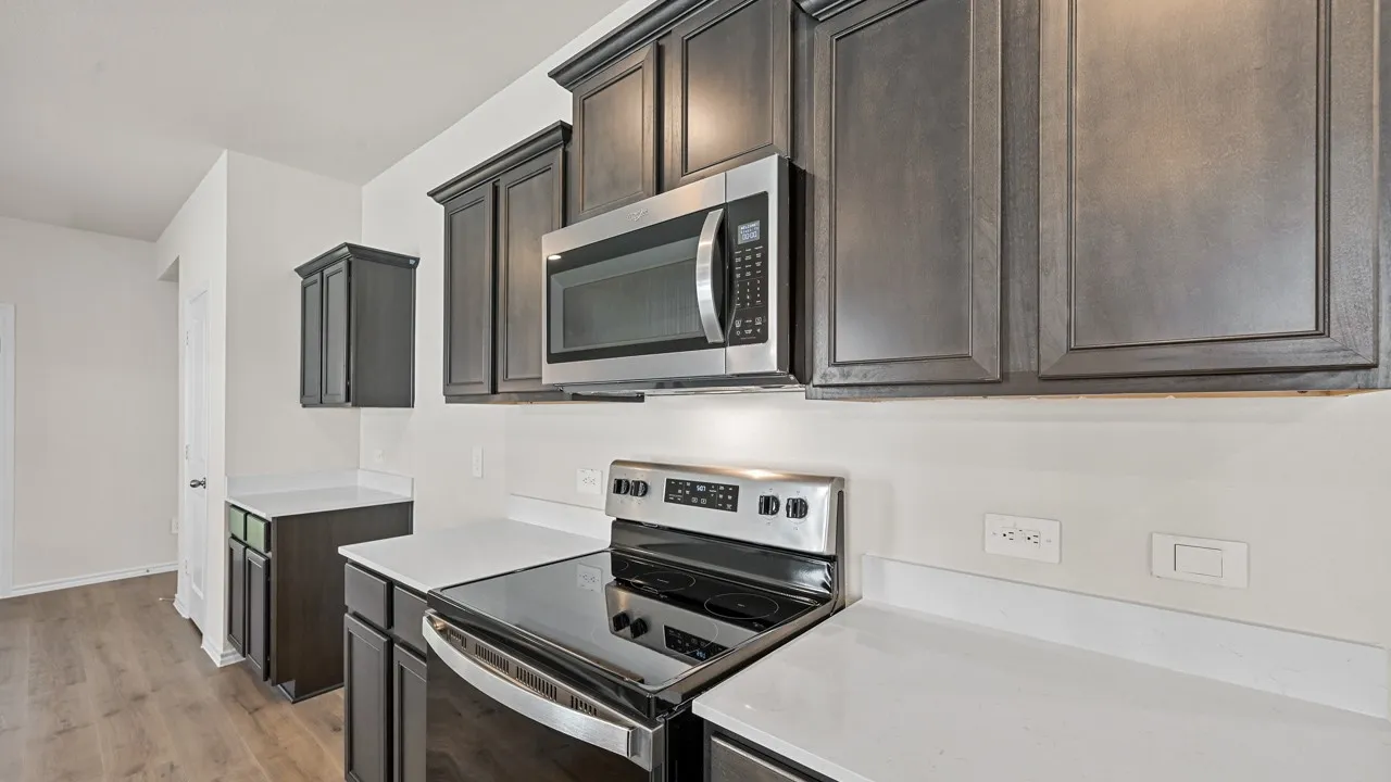 Kitchen featuring dark wood-finish cabinetry, stainless steel microwave, electric range, and white countertops