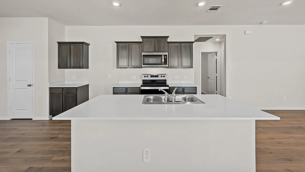 Kitchen island with an undermount stainless steel sink, white countertops, dark wood-finish cabinetry, stainless steel appliances, and recessed lighting