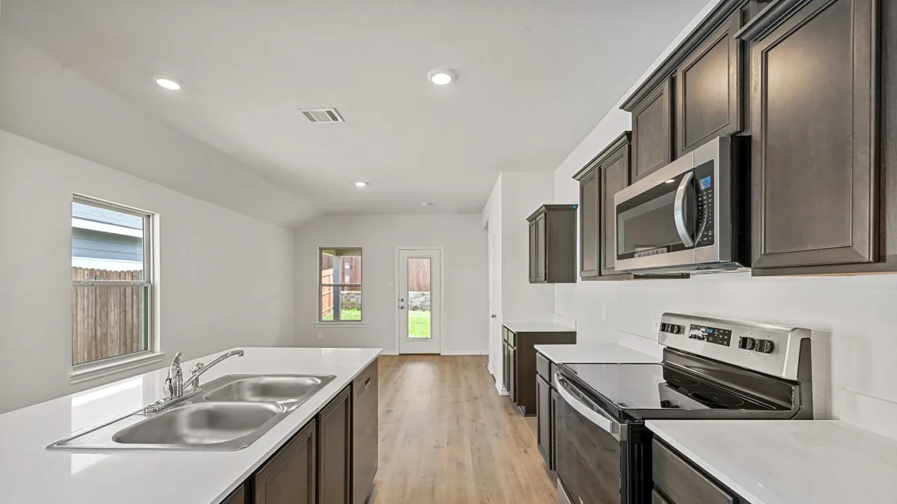 Contemporary kitchen featuring dark wood cabinetry, white countertops, stainless steel appliances, and wood-finish flooring