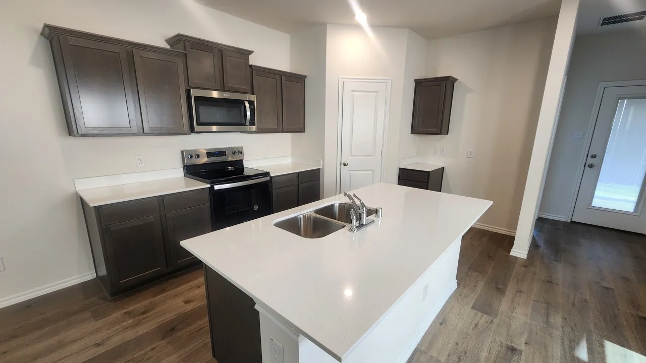 Kitchen featuring a central island with an undermount double basin sink, white countertops, dark wood-finish cabinetry, and stainless steel appliances including an oven with cooktop and a microwave