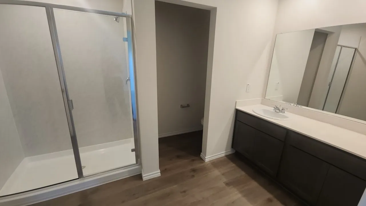 Bathroom featuring a glass-enclosed shower, a vanity with an integrated sink, an expansive mirror, wood-finish flooring, and a separate water closet