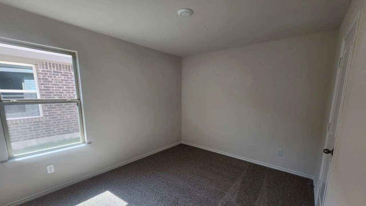 Bright room featuring neutral-toned walls, textured carpet flooring, and a double-hung window with exterior brick exposure