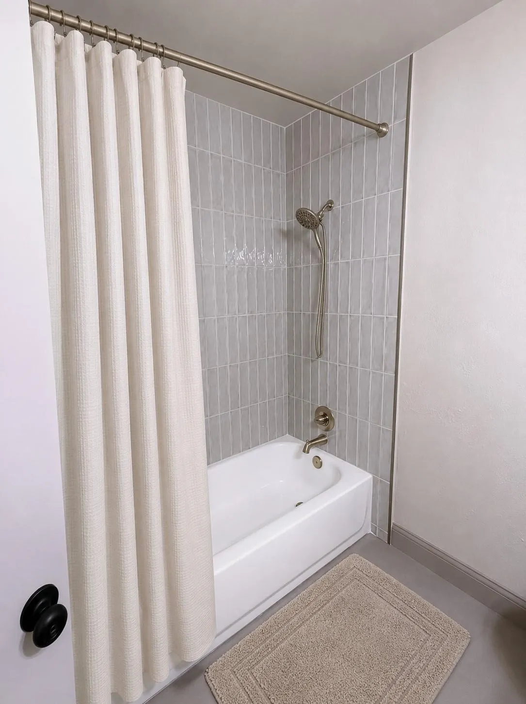 Bathroom featuring a white tub, light gray vertical subway tile surround, brushed nickel fixtures, and a coordinating shower rod
