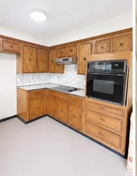 Built-in wall oven with adjacent cooktop, light wood-finish cabinetry, and white marble-look countertops with matching backsplash