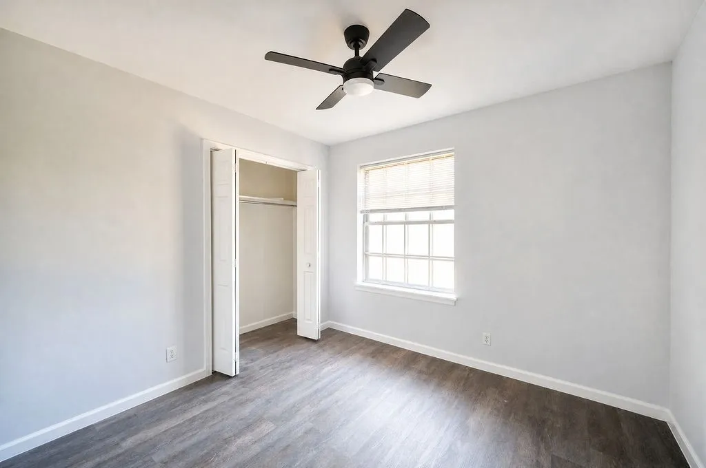 Spacious room featuring wood-finish flooring, a contemporary ceiling fan, and a double-hung window with a window blind