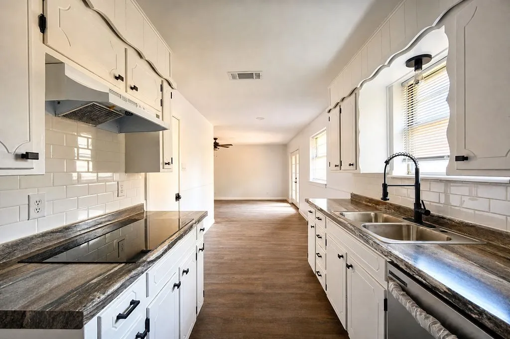 Galley kitchen featuring white cabinetry, subway tile backsplash, a built-in cooktop, dual basin stainless steel sink, and wood-finish flooring