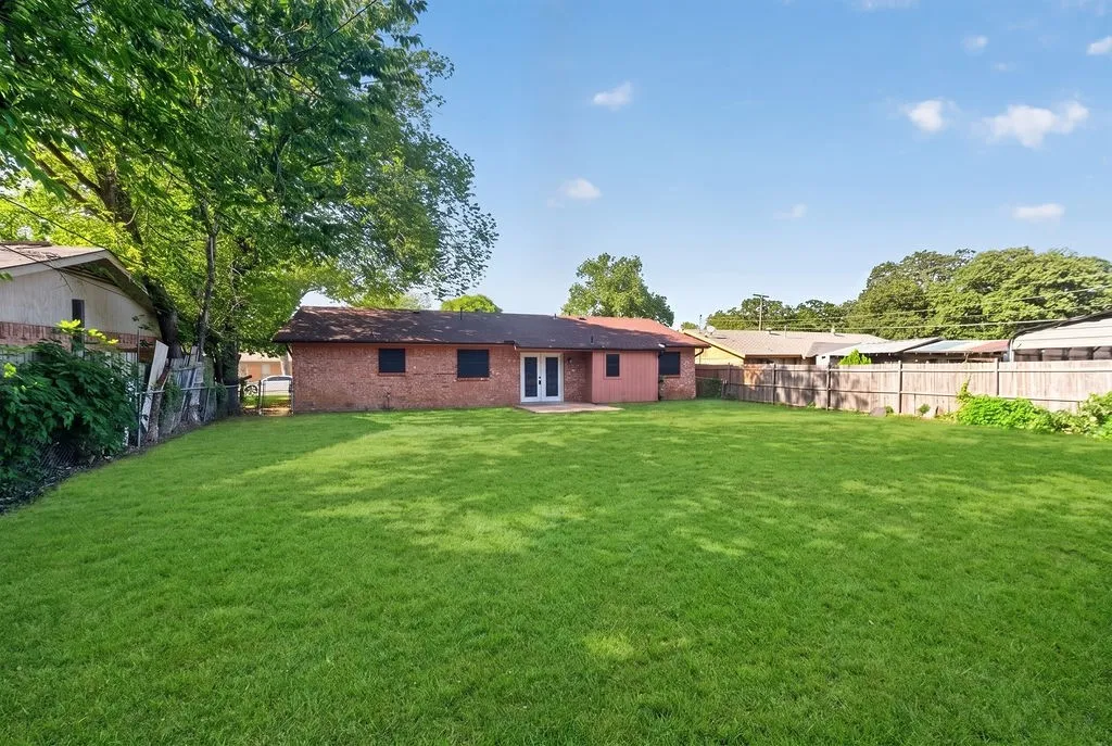 Expansive backyard featuring a large green lawn, perimeter fencing, and mature trees providing natural shade