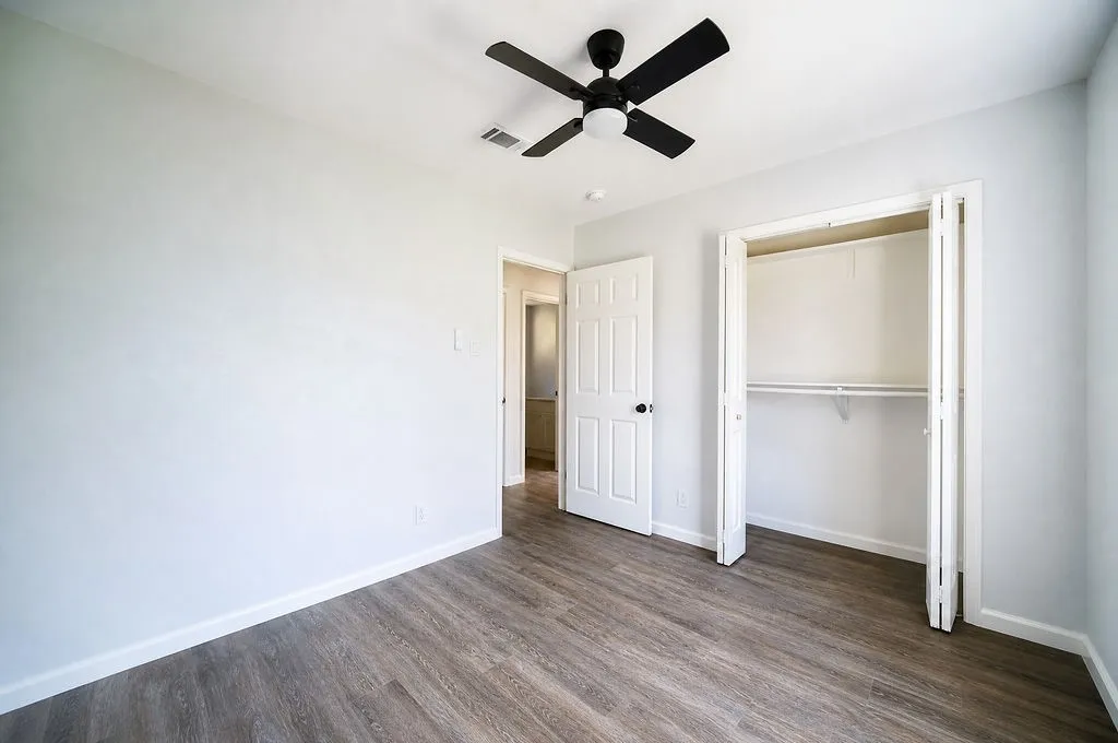 Room featuring wood-finish flooring, a ceiling fan with integrated lighting, bi-fold closet doors, and white baseboards