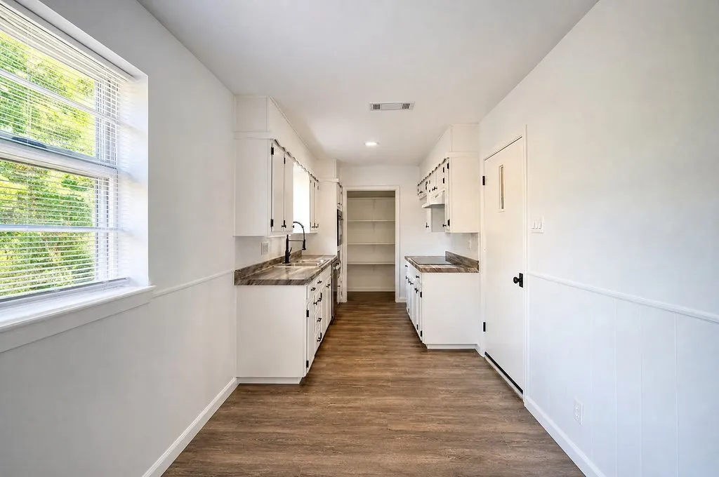 Bright kitchen featuring wood-finish flooring, white cabinetry with dark hardware, stone-finish countertops, and a stainless steel faucet