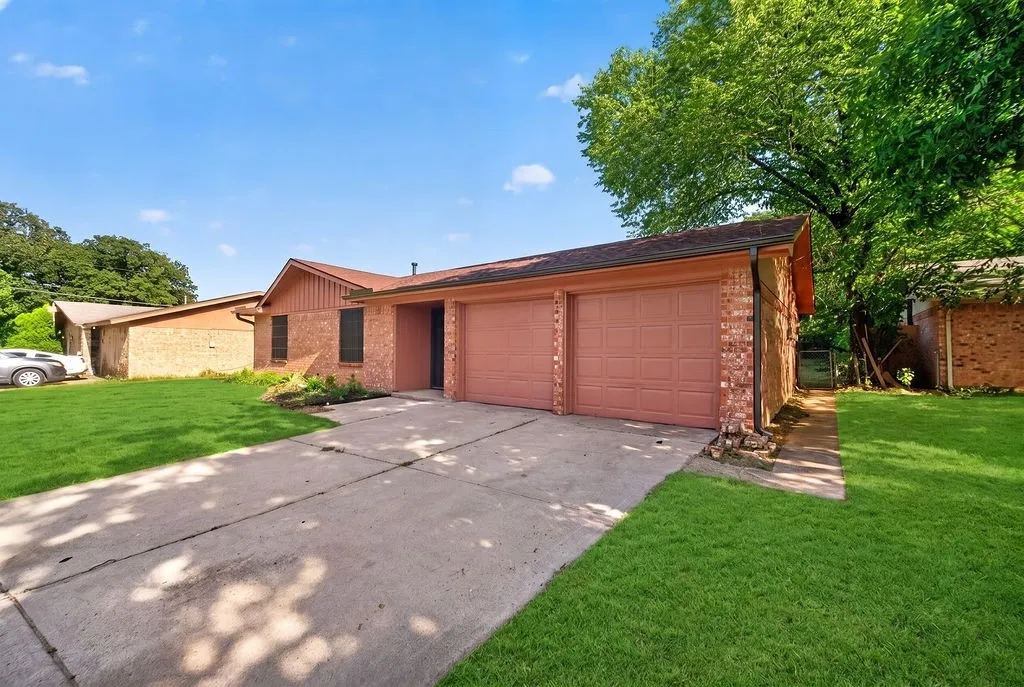 Brick facade residence featuring a two-car garage with panel doors, concrete driveway, and front lawn