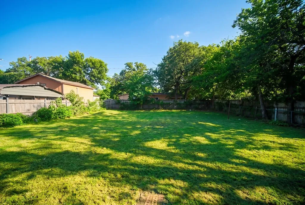 Expansive backyard featuring a lush lawn, mature trees, and privacy fencing