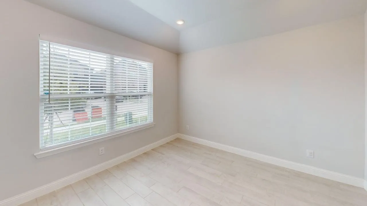 Spacious room featuring a large window with horizontal blinds, light-toned wood-finish flooring, a tray ceiling with recessed lighting, and neutral wall finishes