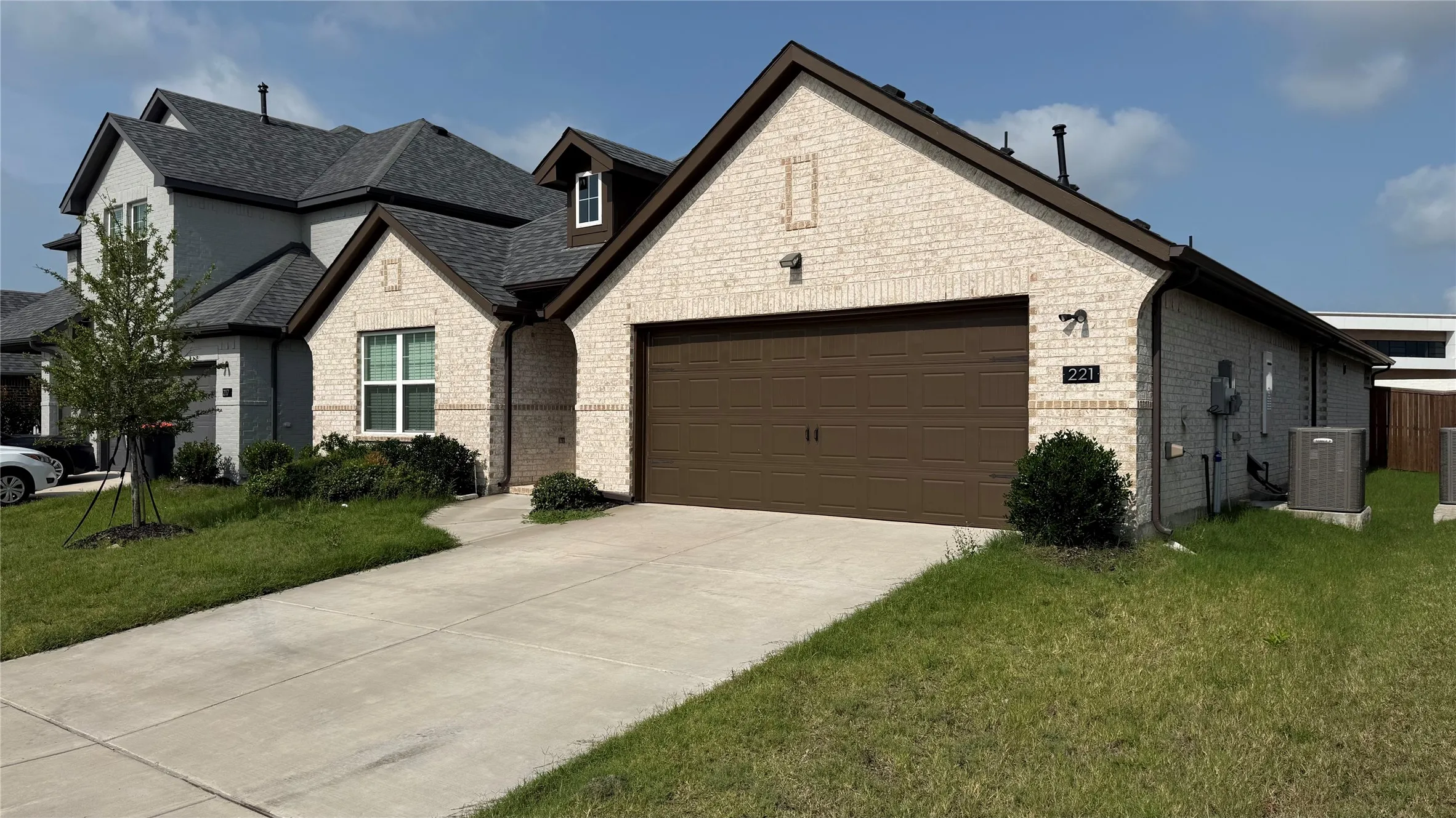 Light-colored brick exterior with dark trim accents, a dark brown garage door, and a concrete driveway